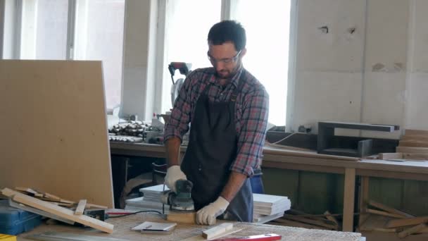 Bearded carpenter working with wooden planck and electric planer in workshop. — Stock Video