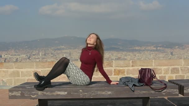 Prendere il sole femminile su una panchina in cima a città — Video Stock