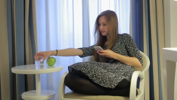 在酒店房间和喝水从玻璃中的智能手机的女孩发短信 — 图库视频影像