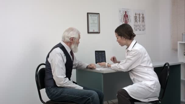 Female doctor reviewing x-ray on a tablet with mature patient. — Stock Video