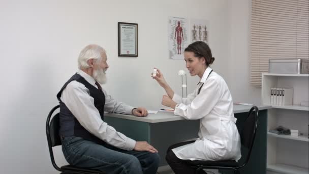 Farmacéutico sonriente sosteniendo un frasco de pastillas y señalándolas a un paciente mayor . — Vídeos de Stock