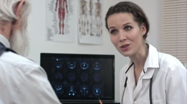 Doktor yaşlı hastalarda MRI taramaları dizüstü bilgisayarda tartışıyor.