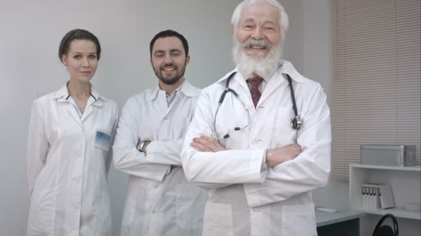 Tres médicos con batas blancas mirando y sonriendo a la cámara . — Vídeos de Stock