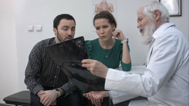 Male Senior Doctor showing a couple a x-ray in a office. — Stock Video