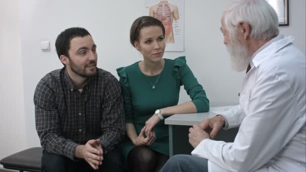 Médecin aîné expliquant quelque chose aux jeunes patients en couple . — Video