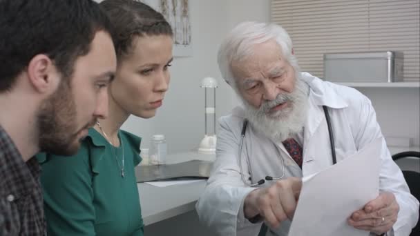 Pareja joven escuchando al médico maduro que les cuenta los resultados de la investigación . — Vídeos de Stock