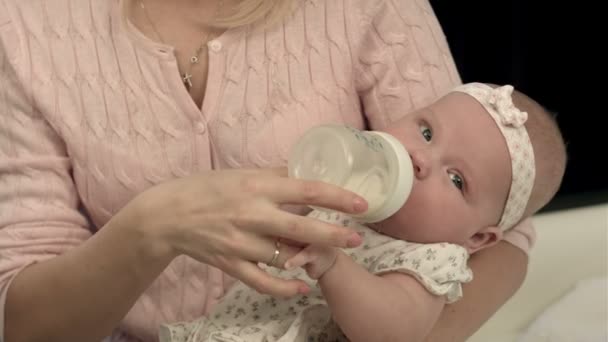 Светлая мать кормит молоком из бутылки своего очаровательного сына дома — стоковое видео