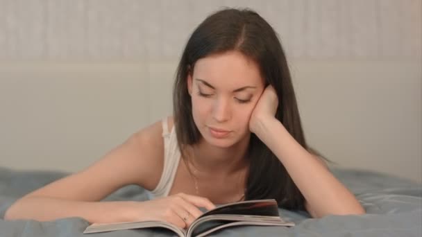Дівчина читає журнал, лежачи на ліжку . — стокове відео