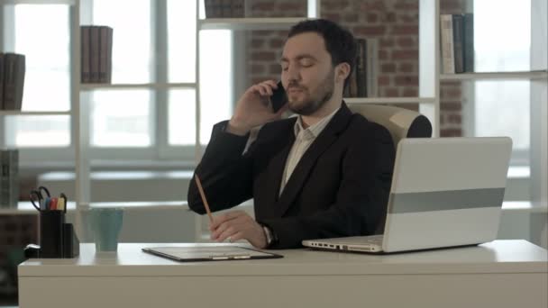 Счастливый улыбающийся молодой человек разговаривает по мобильному телефону в офисе — стоковое видео