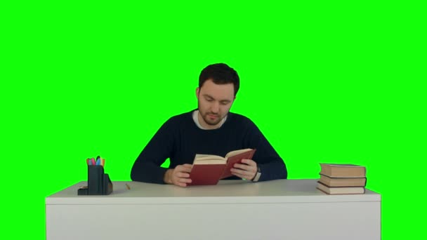 Estudiante joven y concentrado lee un libro en una pantalla verde — Vídeos de Stock