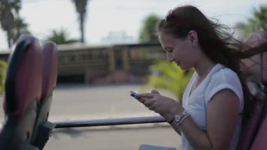 Young beatiful woman traveling by tourist sightseeing bus, with smart phone in sunglasses