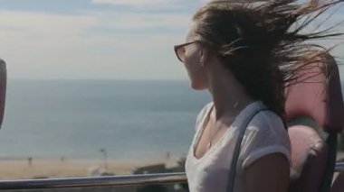 Young beatiful woman traveling thruought coastline with beach and ocean by tourist sightseeing bus, in sunglasses
