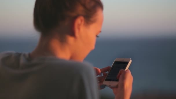 Chica joven de la espalda disfrutando de la vista al mar utilizar el teléfono inteligente — Vídeos de Stock