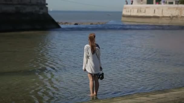 Jeune femme faisant du tourisme, marchant sans chaussures dans l'eau devant le port de l'océan — Video