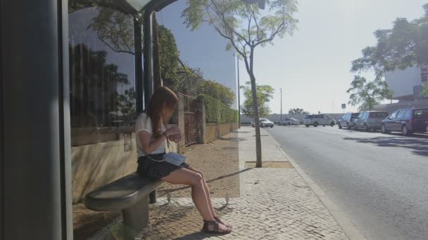 Lisboa, Portugal - Septiembre 2015: Chica joven y solitaria esperando en la parada de autobús en falda azul y gafas de sol, verano, tráfico — Vídeo de stock