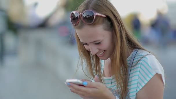 Chica feliz usando un teléfono inteligente en un terraplén de la ciudad sentado — Vídeos de Stock