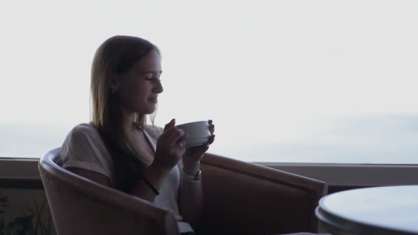 Joven hermosa chica se sienta en un café contemplando hermosas vistas panorámicas del océano atlántico. Mañana con una taza de café, té contemplando — Vídeos de Stock