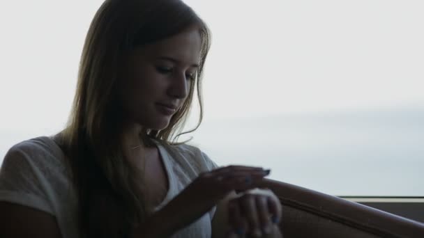 Primer plano de joven hermosa niña se sienta en un café con vistas panorámicas del océano atlántico. Mirando la vista por la mañana — Vídeos de Stock