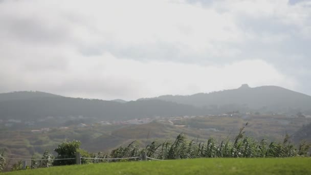 Grönt fält, berg och grå sommarhimmel med moln. blåsigt väder. Landskap vid busstationen i Cabo da Roca Portugal — Stockvideo