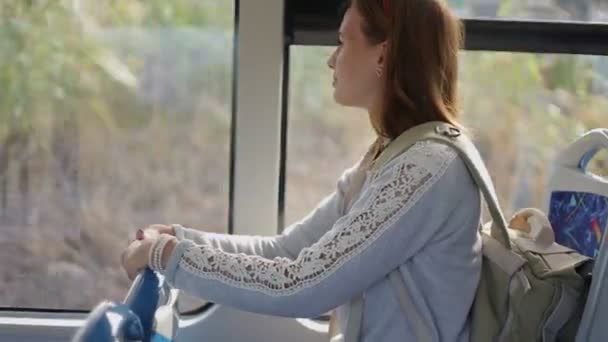 Молодая женщина турист ехать на автобусе с рюкзаком сидит в помещении, глядя в окно — стоковое видео