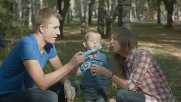 Boy is playing together with his parents. They are playing with soap-bubbles. — Stock Video