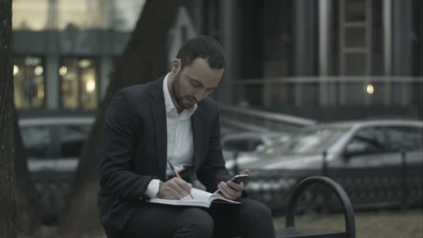 Jovem homem de negócios trabalhando com papéis e telefone no parque verde, esperando por reunião , — Vídeo de Stock