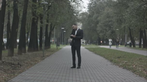 Jonge zakenman in park steegje door de telefoon praten en schrijven in dagboek, werken met notities in het groene park — Stockvideo