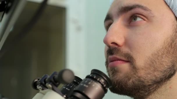 Los ojos del médico barbudo que se cierra en los oculares del sistema de microscopio en un laboratorio médico — Vídeos de Stock
