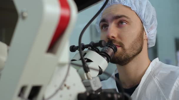 Young doctor using loking at eyepieces of microscope complex system in a hospital laboratory — Stock videók