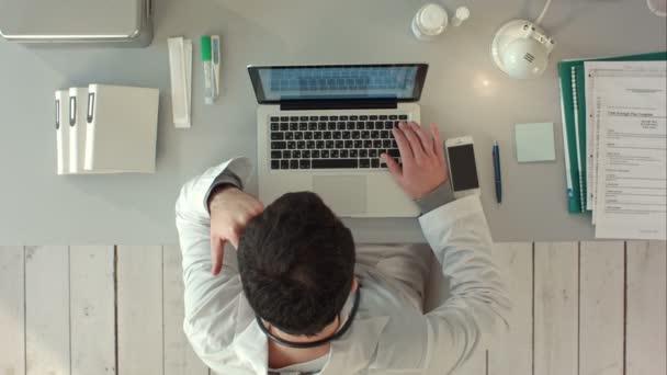 Denkender Arzt mit Laptop in Arztpraxis. Ansicht von oben — Stockvideo