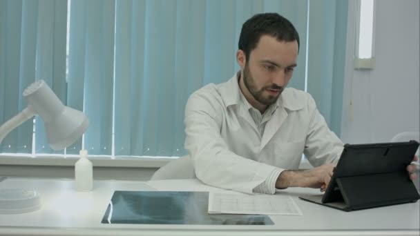 Серйозний молодий бородатий лікар використовує свій цифровий планшет . — стокове відео