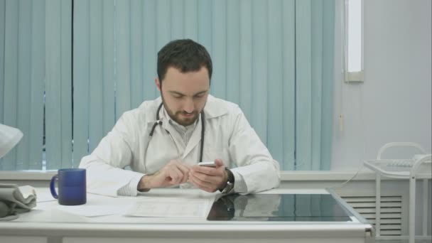 Guapo médico usando teléfono inteligente en el hospital en interiores — Vídeo de stock