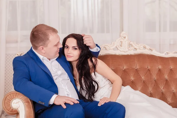 Bride and groom in luxury hotel, kissing on a sofa — Stock Photo, Image