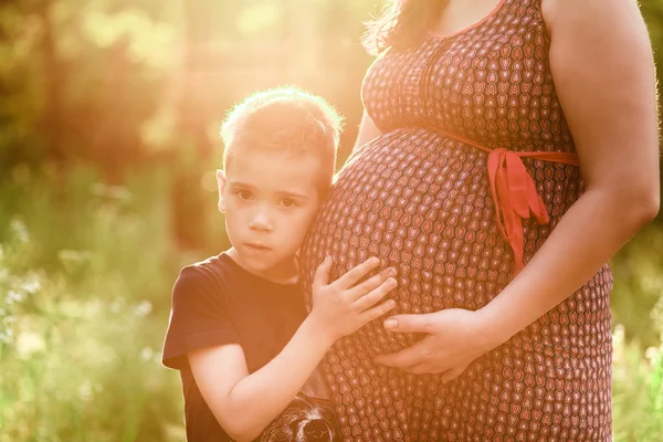 Mały chłopiec całuje brzuch w ciąży matka na zewnątrz — Zdjęcie stockowe