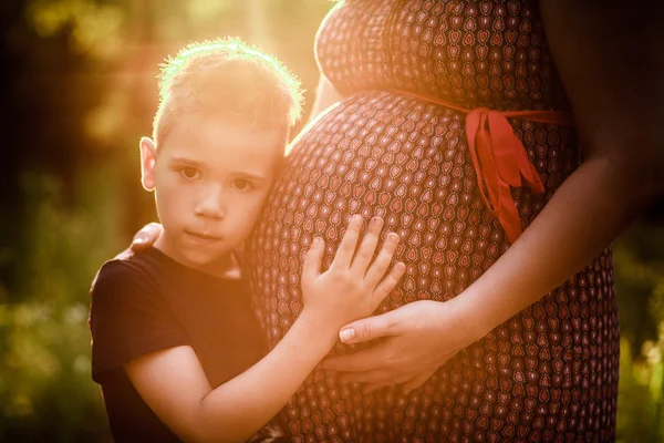 Malý chlapec líbat bříško těhotné matky venku — Stock fotografie