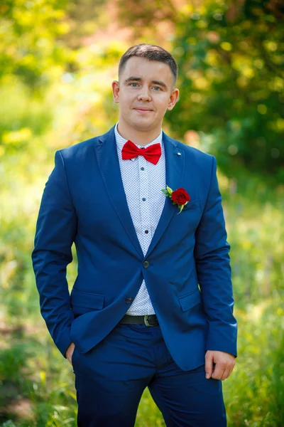 Le marié en costume bleu avec papillon rouge et fleur de boutonnière — Photo