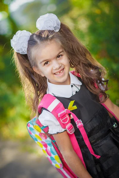 Porträtt av en vacker ung första-grader i festlig skoluniform på bakgrunden hösten park — Stockfoto