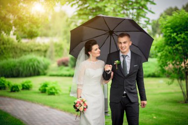 Düğün çift, el ele tutuşarak ve gülümseyen bir parkta duran güzel genç gelin damat