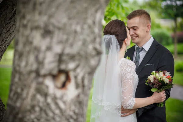 Ζευγάρι γάμος, όμορφη νεαρή νύφη γαμπρός στέκεται σε ένα πάρκο, κρατώντας τα χέρια και χαμογελαστός — Φωτογραφία Αρχείου