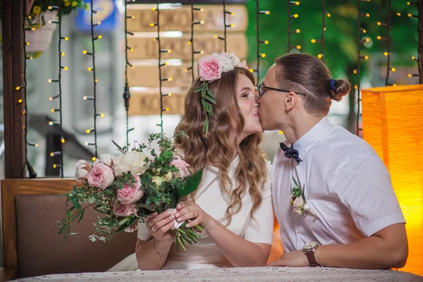 Feliz pareja sonriente recién casada sentada y besándose en la terraza con ramo — Foto de Stock