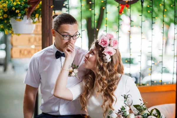 Feliz casal recém-casado sorridente sentado e beijando no terraço com buquê — Fotografia de Stock