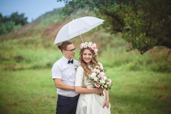 Noiva e noivo sorriem abraçando sob um guarda-chuva branco — Fotografia de Stock