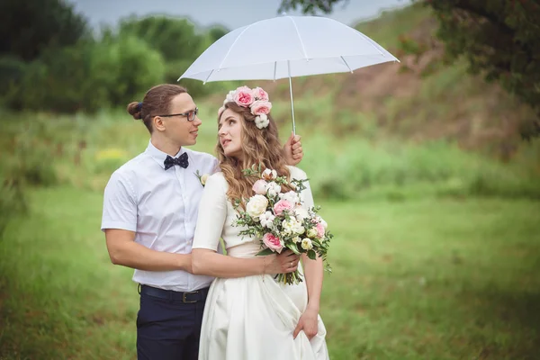 Bride and groom smile hugging under a white umbrella — Stock Photo, Image