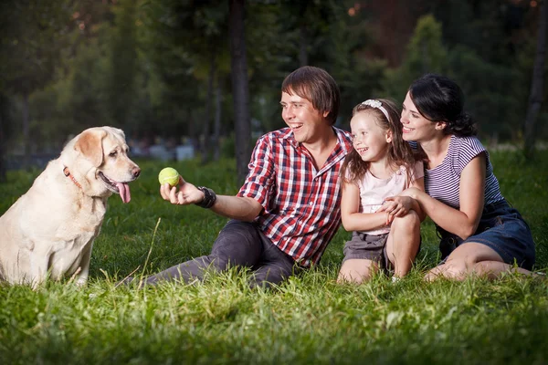 Familia sentada en la hierba con el perro — Foto de Stock