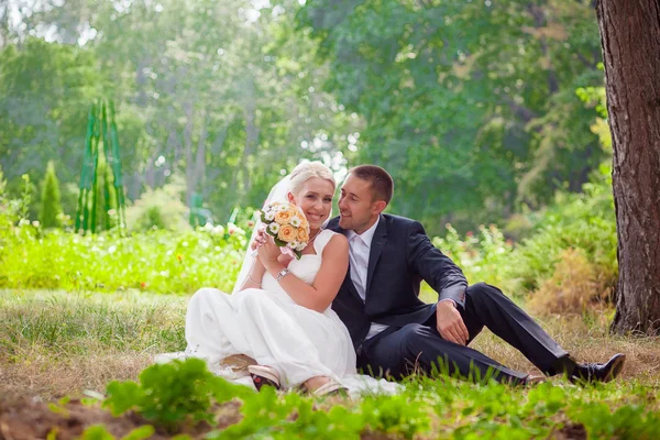 Brudparet sitter på gräset i parken — Stockfoto