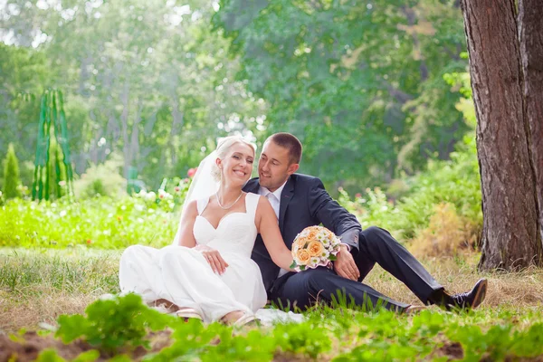 Bruid en bruidegom zitten op gras in het park — Stockfoto