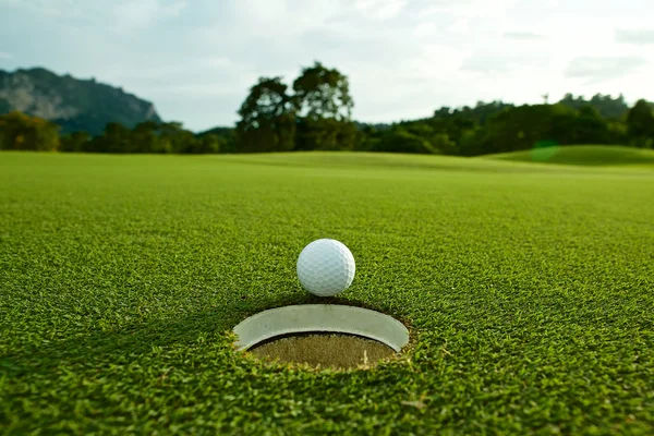 Utflytning ljus foto av vita golfboll nära hål på fairway w — Stockfoto