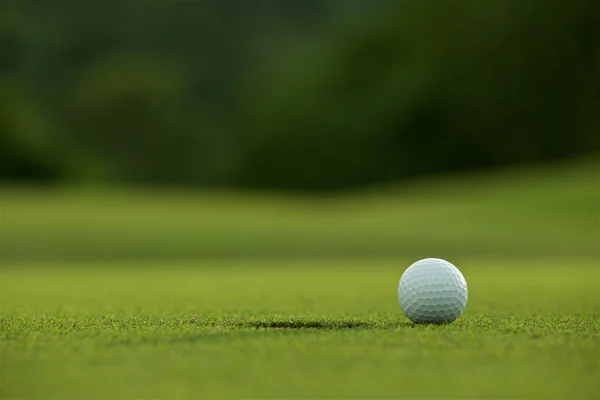 Vit golf boll nära hål på fairway med grön bakgrund i — Stockfoto