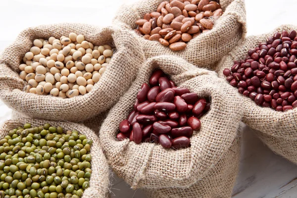 Assortiment de haricots et lentilles dans le sac de chanvre sur fond de bois — Photo