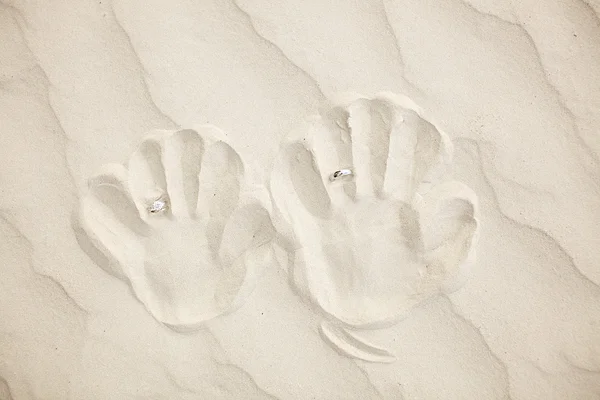 Wedding rings with handprint on the white sand — Stock Photo, Image